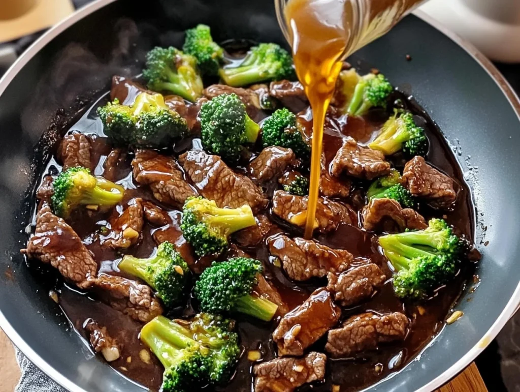 Beef broccoli stir-fry cooking in a skillet with tender beef, crisp broccoli, and savory sauce being poured over for a flavorful and quick dinner.