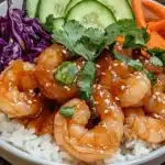 A delicious honey sriracha shrimp bowl with tender shrimp coated in a sweet and spicy glaze, served over fluffy rice with fresh vegetables like cucumbers, carrots, and purple cabbage.