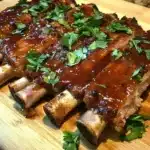 Tender, fall-off-the-bone honey garlic ribs coated in a rich, glossy glaze, served on a wooden platter with a side of fresh herbs.